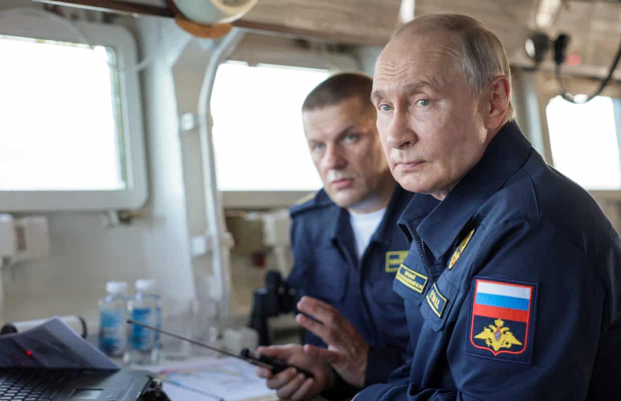 In naval fatigues, Vladimir Putin sits alongside Adm Viktor Liina on the bridge of a navy ship