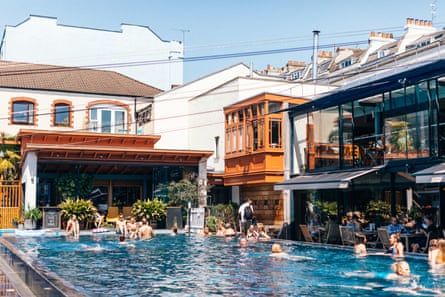 Swimming pool at hotel with bar surrounded by buildings on sunny day.