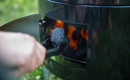 A hand is seen putting coal into the Bar-Be=Quick Smoker & Grill barbecue