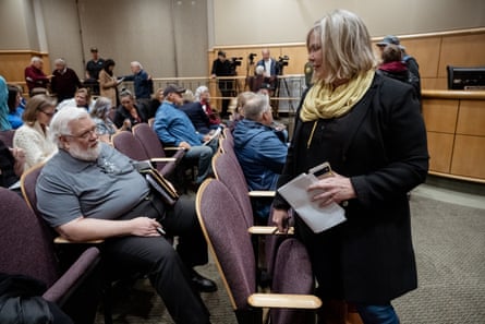 woman wearing yellow scarf and black coat stands by people sitting in rows of seats