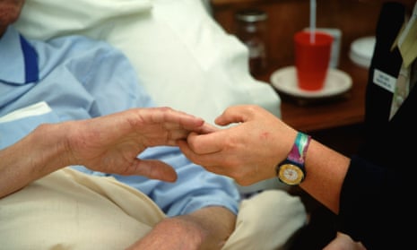 A hospice worker holds the hand of a patient.