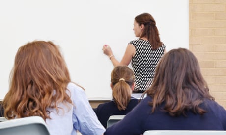 Primary school teacher writing on a clear whiteboard in a classroom