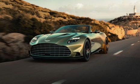 An Aston Martin car driving down a road at sunset