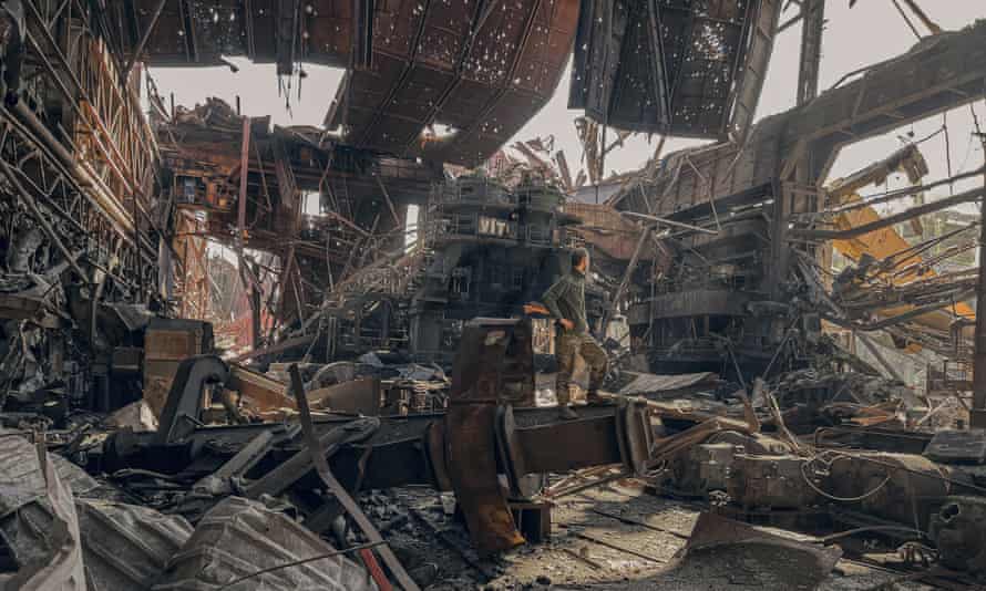 Un soldado se para en las ruinas de una habitación hecha jirones llena de escombros y con la luz proveniente de paredes, techos y otros agujeros de proyectiles destruidos.