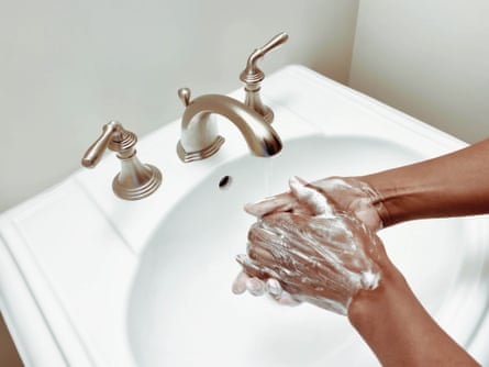 Woman lathers soap on hands at a white sink.