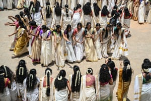 Women standing in a circle and facing outwards performing a dance as others watch