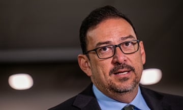 Middle-aged Latino man with dark hair, glasses, wearing suit.
