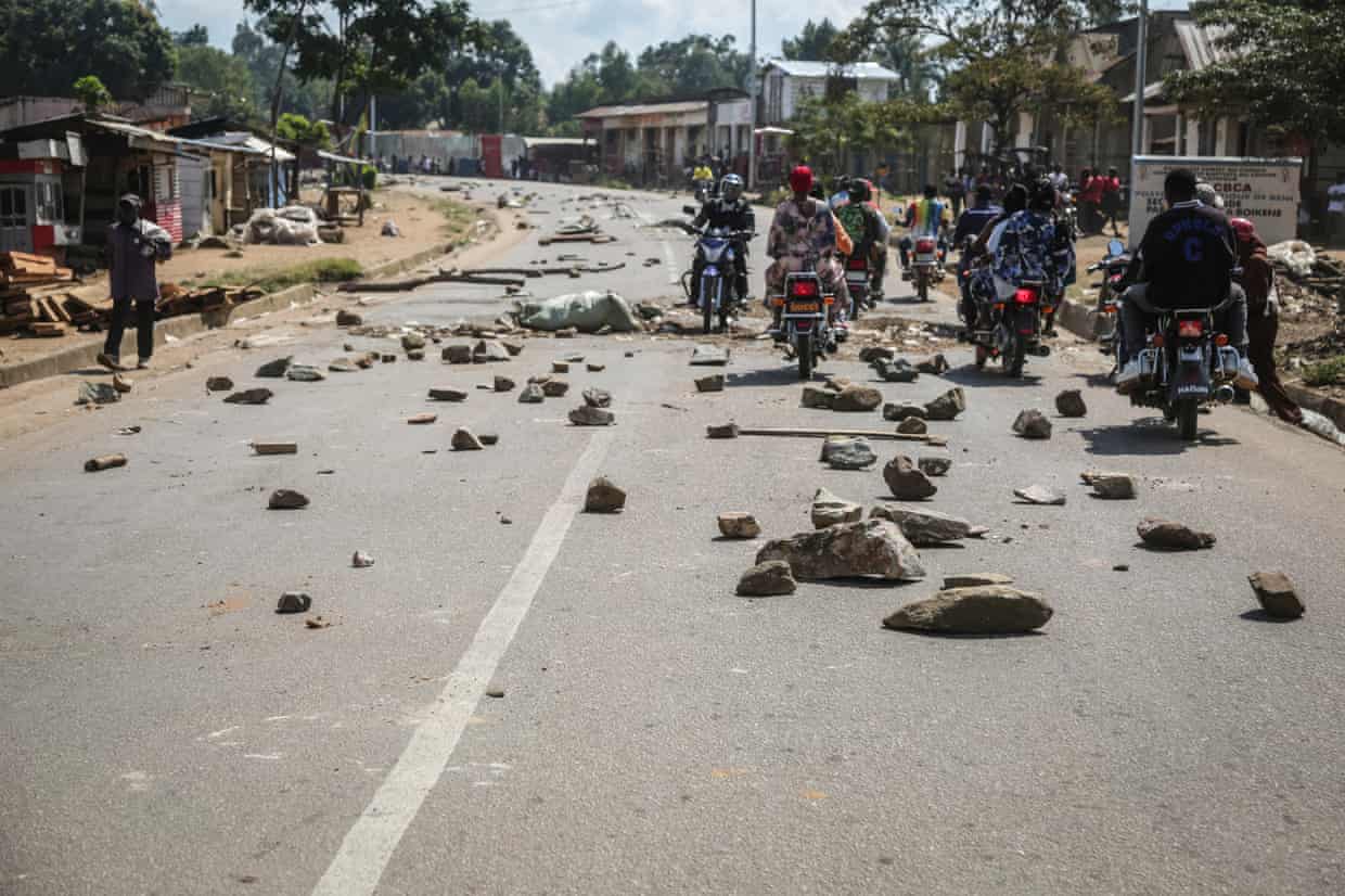 A group of motorcyclists ride along a road littered with stones and other debris