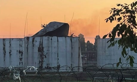 An image showing a large piece of twisted sheet metal and smoke at the top of an industrial building, with razor wire in the foreground