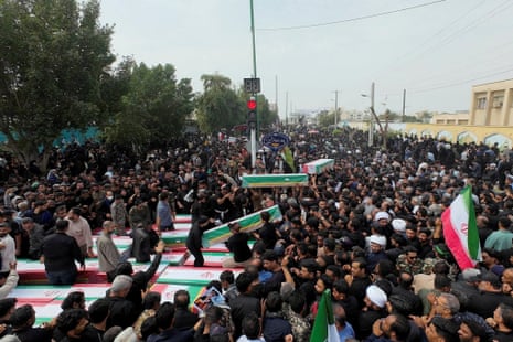Large crowds of people surround coffins draped in Iranian flags.
