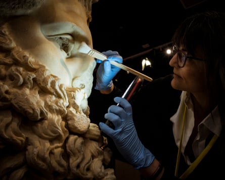 A conservator with a torch and brush tends to a huge representation of Zeus's head