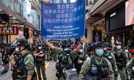 A riot police officer holds up a blue flag letting protesters know they are infringing the law by with a banned protest in Hong Kong on 1 october 2020