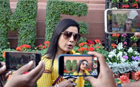 Mahua Moitra in the garden at the Parliament House complex, New Delhi – she is standing in front of bright flowers while people photograph and film her on their phones, and is wearing large sunglasses and a yellow top