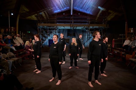 Actors of quite diverse ages and sizes wearing black sweatshirts and trousers stand barefoot in a circle facing outwards in the centre of the theatre space.
