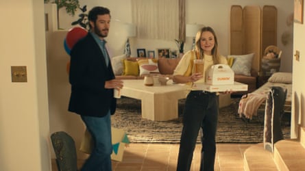A man and a woman walk into a room holding Dunkin Donuts cups and boxes