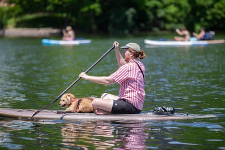 A man paddleboards with his dog with kayaks in the background.