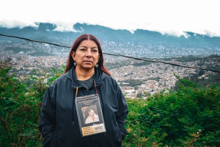 A middle-aged woman with a photo of a man attached to a lanyard around her neck.