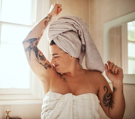 Shot of a woman with a towel on her head and one on her body, smelling her armpits during her morning beauty routine