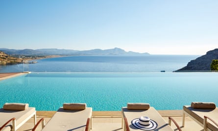 Des chaises longues donnent sur une piscine, puis sur une petite baie océanique vers des terres lointaines.