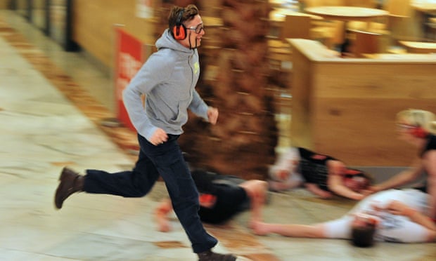 An actor playing the part of a shopper runs for cover.