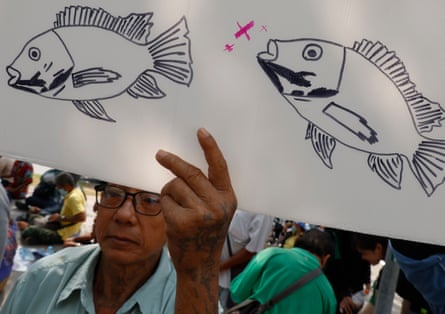 A Thai fish farmer holds a banner with a drawing of a blackchin tilapia fish during a demonstration