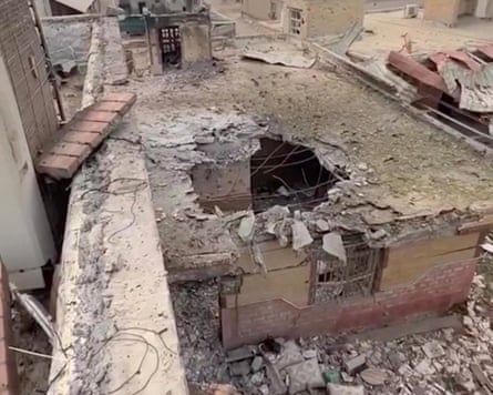 Overhead view of a flat-roofed house with a bomb hole in the roof surrounded by rubble.