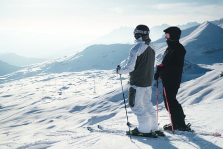 Two skiers stand and look down on a snowy mountainous landscape on a clear day