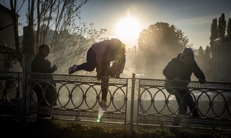 People jump over a fence after drone strike in Kyiv as more drones fly overheard.