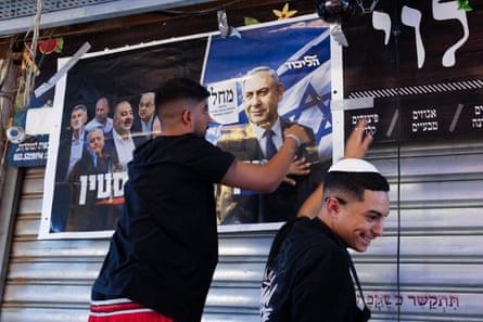 A supporter tapes up a poster of Netanyahu on a market shutter as another man smiles nearby