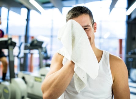 Man wiping his sweat from face with towel after exercising in gym