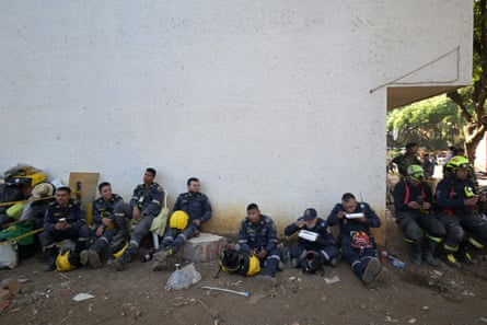 Half a dozen people, some with yellow hard hats sit beside white wall