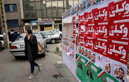 An Iranian woman walks past electoral posters in Tehran