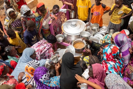 People gather around a table with large vats of food on it.