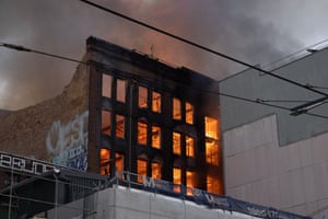 A blackened outer wall of the building with orange flames visible through the windows