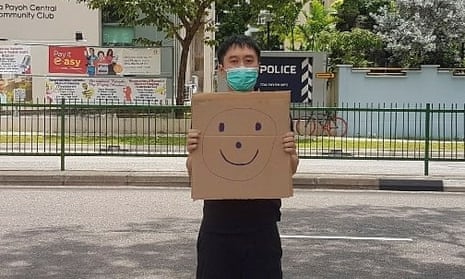 Jolovan Wham wears a mask and holds a cardboard with a drawing of a smiley face outside a Singapore police station in March.