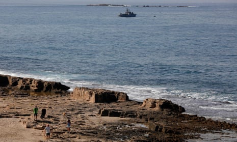 People walk along a beach in Lebanon as an Israeli navy vessel patrols offshore