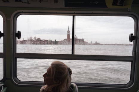 A woman seated on a vaporetto, the tower of St Mark’s Basilica visible through the window behind her