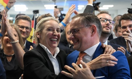 Alice Weidel and Tino Chrupalla celebrate: they have their hands on each other’s shoulders and are smiling as a crowd of people, some holding German flags, clap and wave their arms behind them.