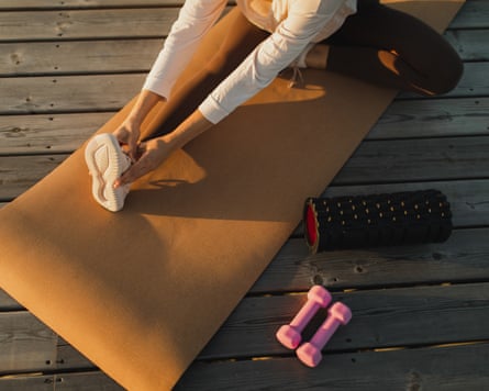 Female athlete stretching on yoga mat before outdoors workout with dumbbells and foam roller