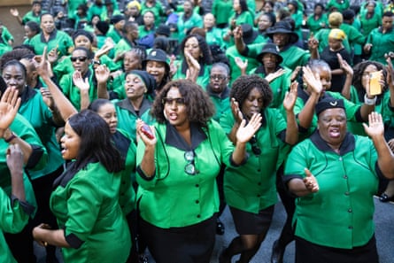 A large group of black African women in green shirts sing and clap