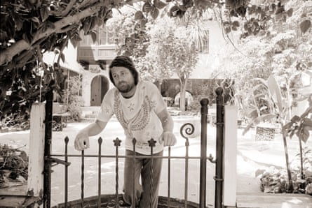 sepia-toned photo of man wearing white shirt and jeans leaning against railing