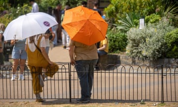 Two people lean against a metal fence and hold up white and orange umbrellas