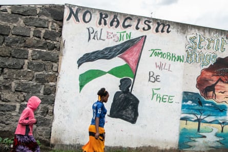 People walk past a mural featuring a Palestinian flag and the words ‘No racism Palestine, tomorrow will be free’