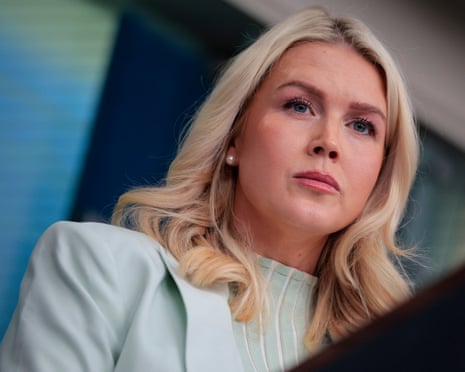 Karoline Leavitt stands at a podium as she listens to a reporter’s question