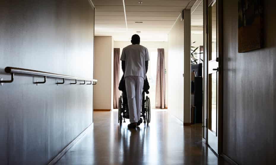 A man pushing a person in a wheelchair down a corridor