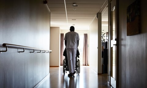 A worker pushes a person in a wheelchair down a corridor