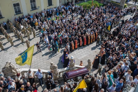 Photograph from a high position of Andrew Parubiy’s coffin being carried up steps as a crowd watches from behind ranks of service personnel and clerics