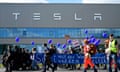 Environmentalists march in front of a Tesla plant, carrying blue protest banners and balloons