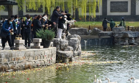 People stand on the edge of a wide river and throw petals into the water.