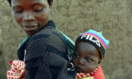 An African woman looks back at the baby son, wearing a knitted cap, strapped to her back